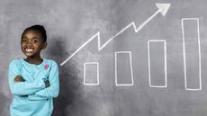 young girl in teal shirt standing by chalkboard with bar charts and arrow going up