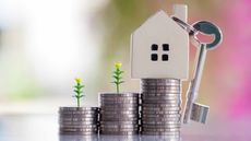 tiny house with key sitting on stacks of coins