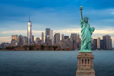 The statue of Liberty with Downtown New York skyline panorama with Ellis Island in the foreground at night in New York City, USA