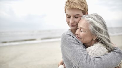 An adult daughter hugs her mom on the beach.