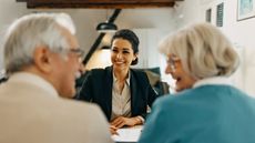 A financial adviser smiles across her desk at her older clients. 