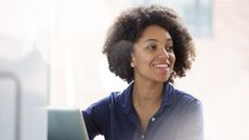 A young woman smiles as she sits at her desk in an office.