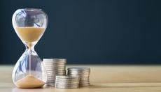 hourglass next to three stacks of coins on wooden table