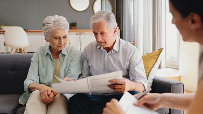 An older couple look at paperwork while sitting on a sofa in a financial planner's office.